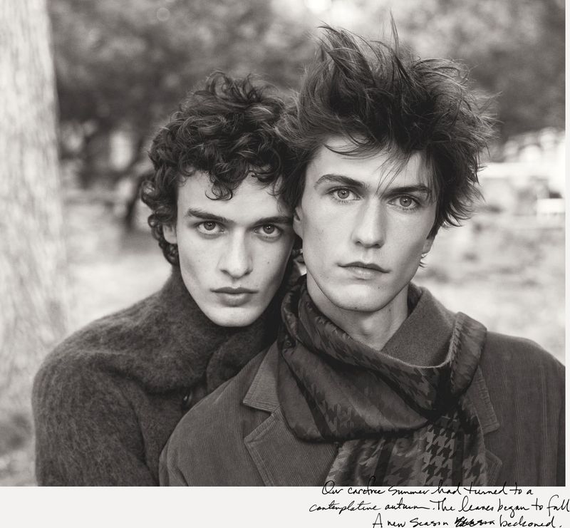 Black and white portrait of two young adult men outdoors, posing in soft light, wearing jackets and scarf, exuding a contemplative mood.
