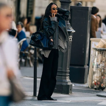 A woman in a black leather jacket and sunglasses standing on a city street holding a handbag