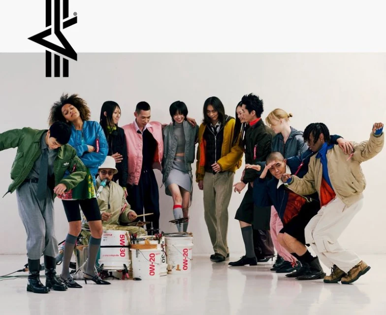 Group of diverse adults in fashionable jackets and outfits posing in front of a white background, with a drummer and paint bucket drums.