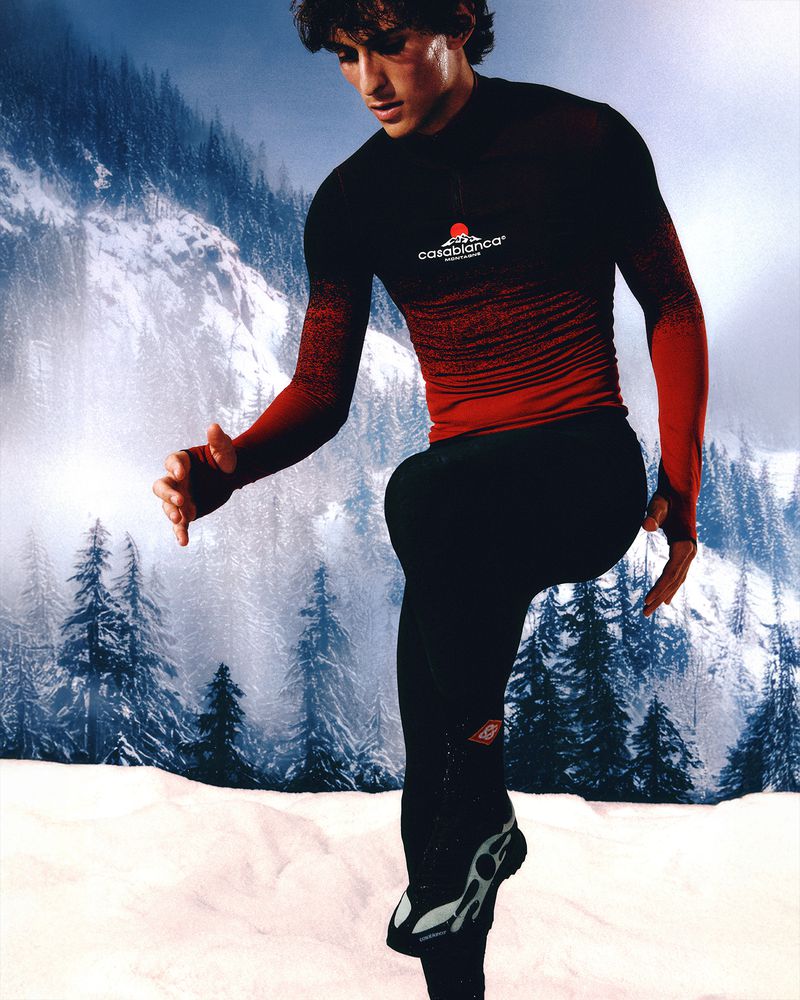 Athletic man in black and red sportswear stretches in a snowy mountain landscape, creating a dynamic, sporty, and natural image.