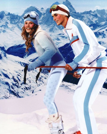 A couple in matching ski outfits, posing on the snowy slopes of a mountain, showcasing winter fashion in a bright, outdoor setting.