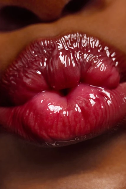 Close-up of red glossy lips on dark skin, highlighting texture and color. Shot at eye-level to showcase lip detail and beauty.