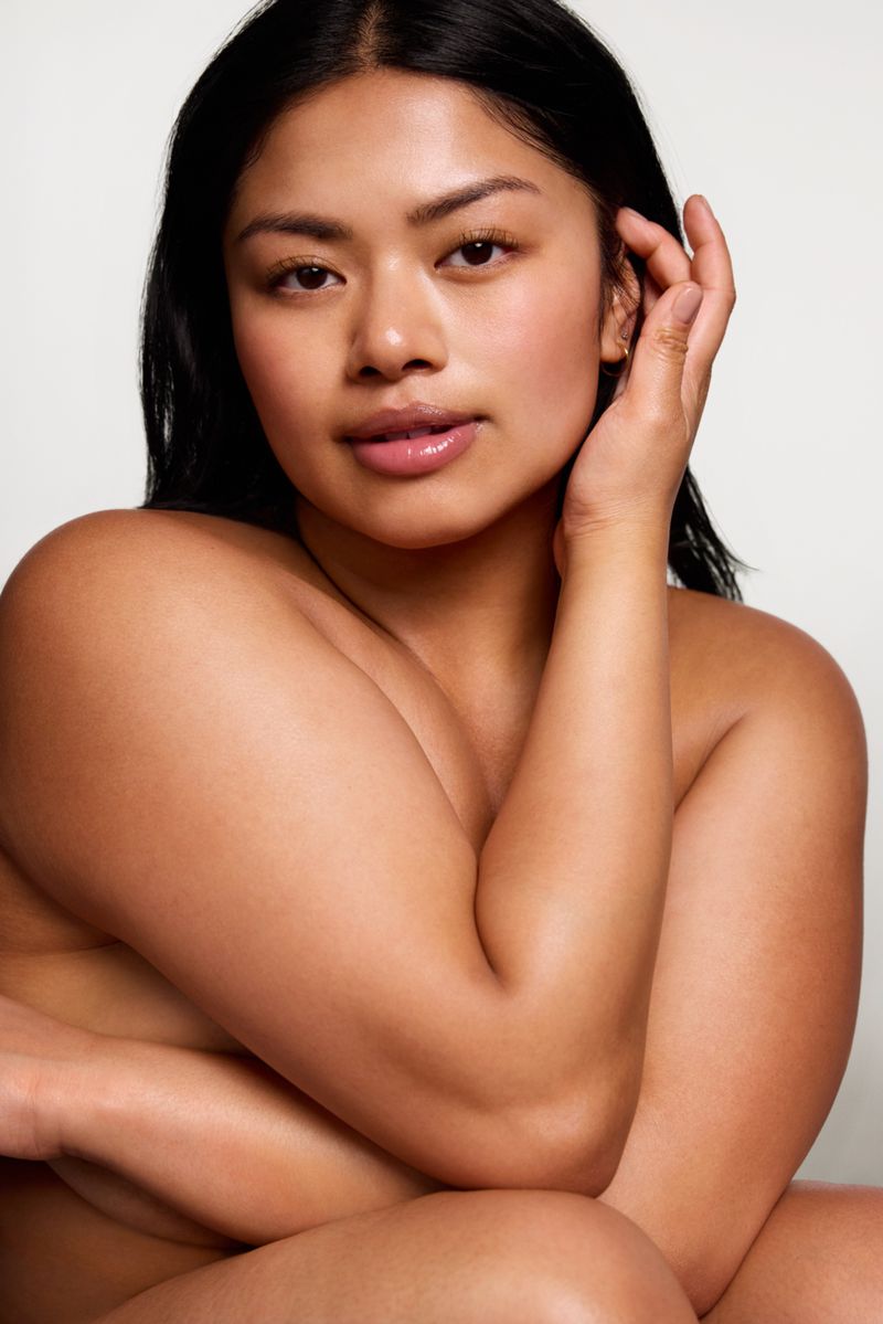 Portrait of an adult woman with bare shoulders, soft lighting, and a neutral background. She has dark hair and light skin.