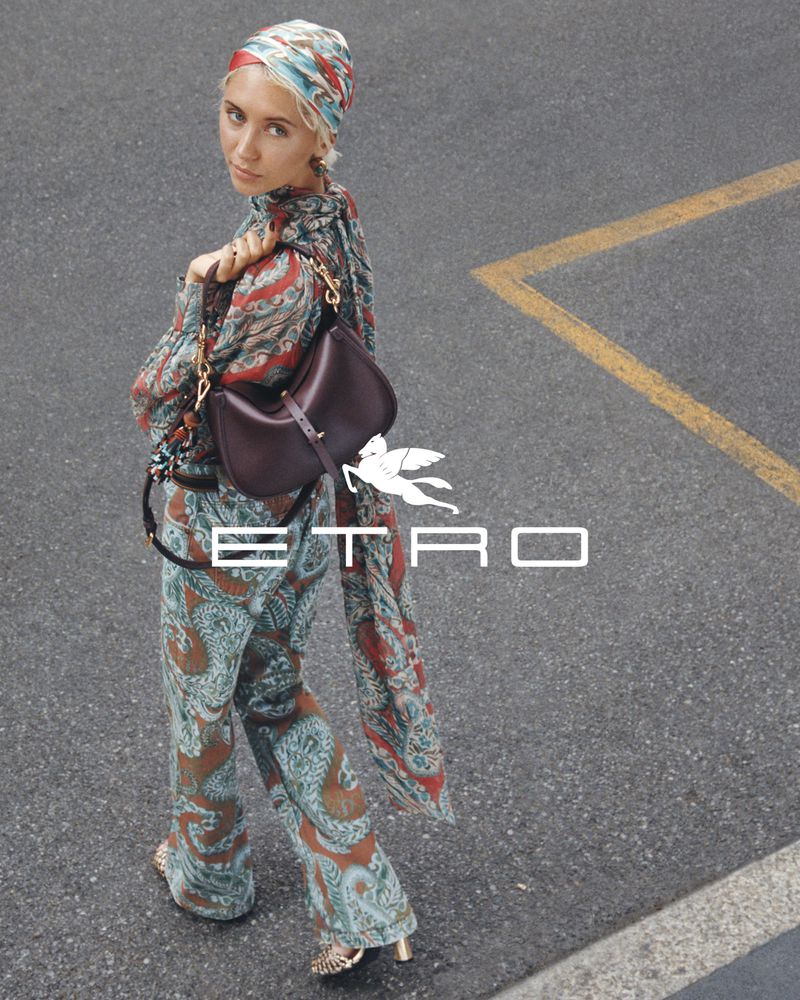 Fashion shot featuring a woman with a headscarf, patterned top and pants, a brown purse, and Etro logo text on a city street.