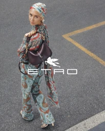 Model Iris Law wearing patterned clothing and a matching headscarf while holding a dark leather shoulder bag on an asphalt street