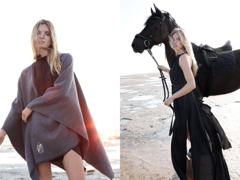 Fashion shot of two fair-skinned women in fashionable garments, one standing next to a dark horse, in an outdoor sandy setting.
