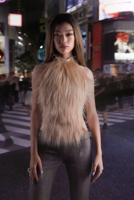 Adult Asian woman posing in a fur top and glittering pants in an urban scene at night with bokeh and blurred lights.
