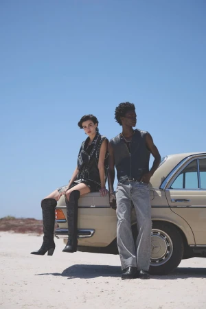 A woman seated on a vintage car hood and a man standing beside it against a clear sky background