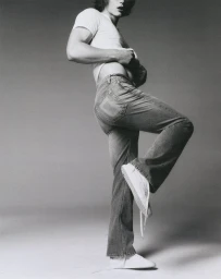 Man wearing a white t-shirt and denim jeans posing against a grey seamless studio background for Calvin Klein.