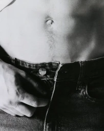 Close-up of a person unbuttoning blue denim jeans, focusing on the waistline and hand