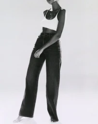 Monochrome fashion image of a model wearing a white tank top and high-waisted dark jeans against a white backdrop.