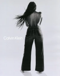 Model with long braided hair wearing dark denim jeans posing against a white background for Calvin Klein.