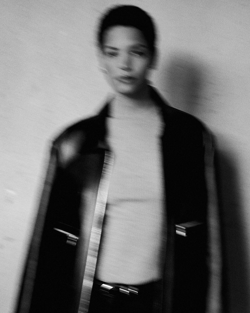 Monochrome portrait of a woman in a jacket against a blurred white backdrop with intentional blur, creating an abstract, stylized visual.