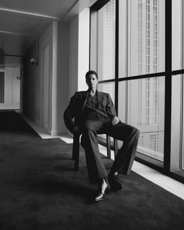 Model wearing a tailored suit seated on a chair next to large windows in an interior hallway for Alex Eagle AW 25 Everyday Rhythm.