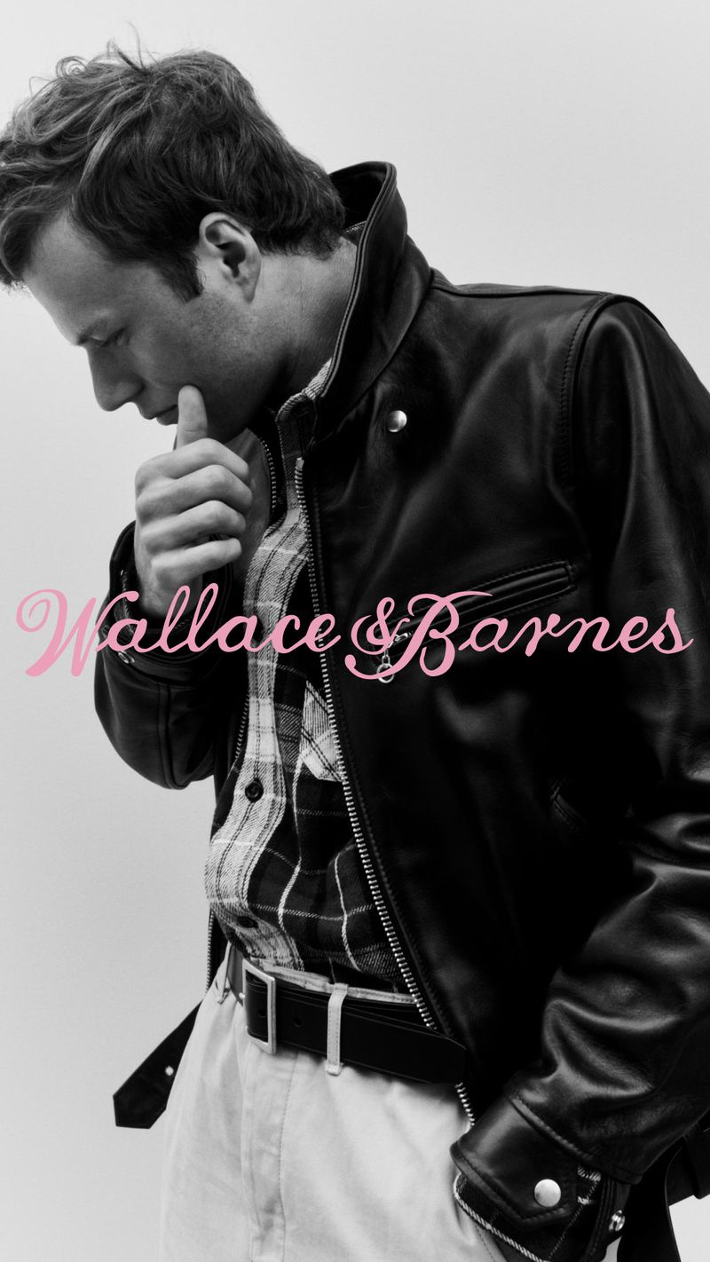Man in black leather jacket, plaid shirt, and white pants in a vertical studio shot, showcasing fashion and style.
