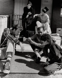Monochrome lifestyle editorial showing a group of men gathered outdoors playing dice on a sidewalk
