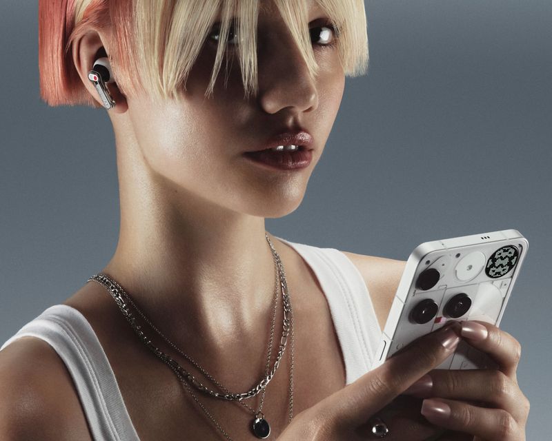 Close-up of a woman with short, blonde hair holding a phone and wearing wireless earbuds, showcasing technology and modern fashion.