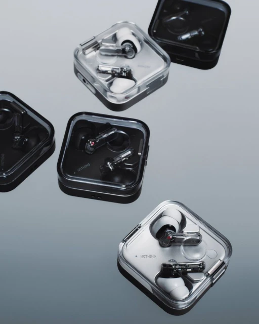 Several black and white wireless earbuds in transparent charging cases are displayed on a reflective gray surface in a studio setting.