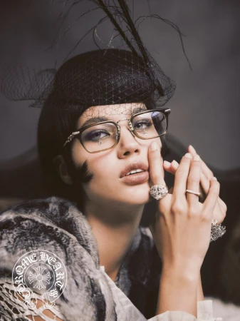 Portrait of a woman wearing glasses and a black feathered hat. She has rings on her fingers and is wearing a fur stole.
