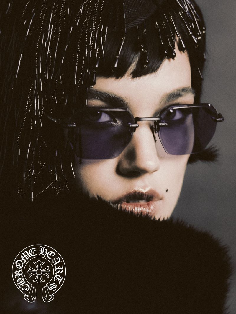 Close-up portrait of a fashion model wearing sunglasses and a beaded headpiece, showcasing dark fur clothing and Chrome Hearts logo.