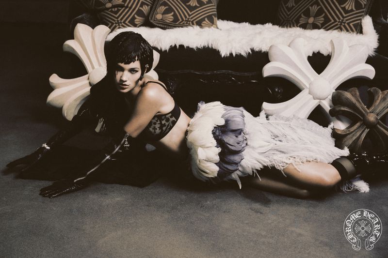 Fashion photo of an adult woman in lingerie and black gloves lying on the floor, with decorative crosses and a dark couch.