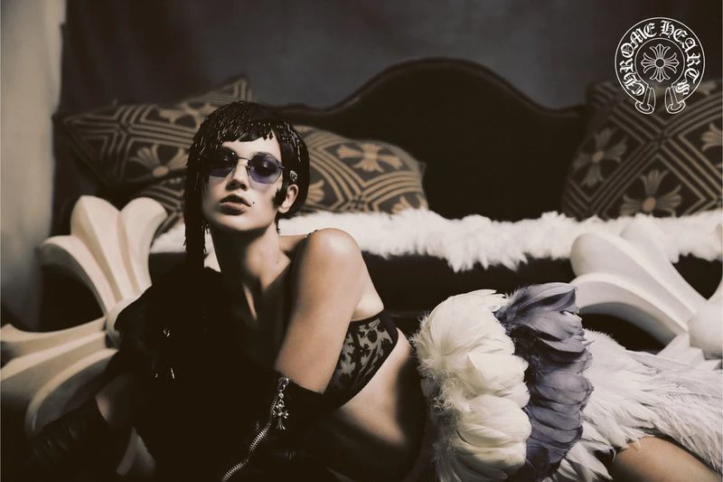 Model wearing dark sunglasses and lingerie reclining on a sofa with feather trim, for Chrome Hearts S/S 25 campaign.
