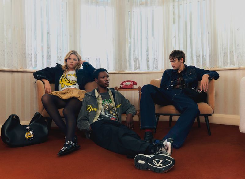 Three young adults in fashionable clothing sit in armchairs inside a room with white and brown striped walls and sheer white curtains.