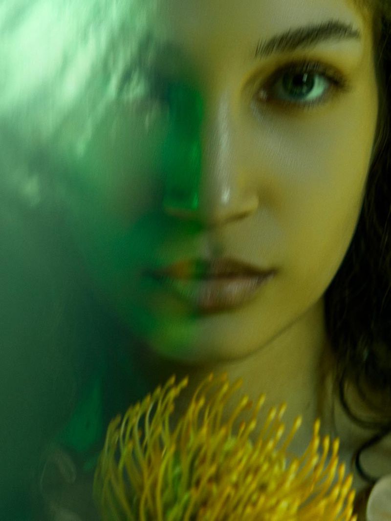 Close-up portrait of a young woman with yellow flower under creative green and yellow lighting, soft focus lens, beauty concept.