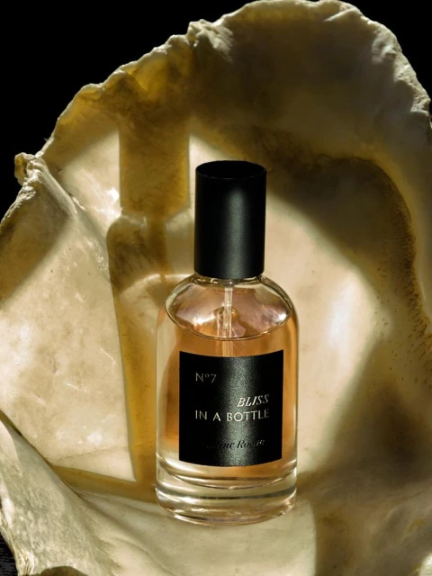 Close-up of a perfume bottle on a seashell, highlighting the bottle's label and the texture of the shell against a dark background.