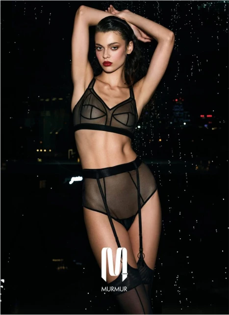 Elegant woman in lingerie posing against an out-of-focus cityscape at night, showcasing a modern and alluring aesthetic.