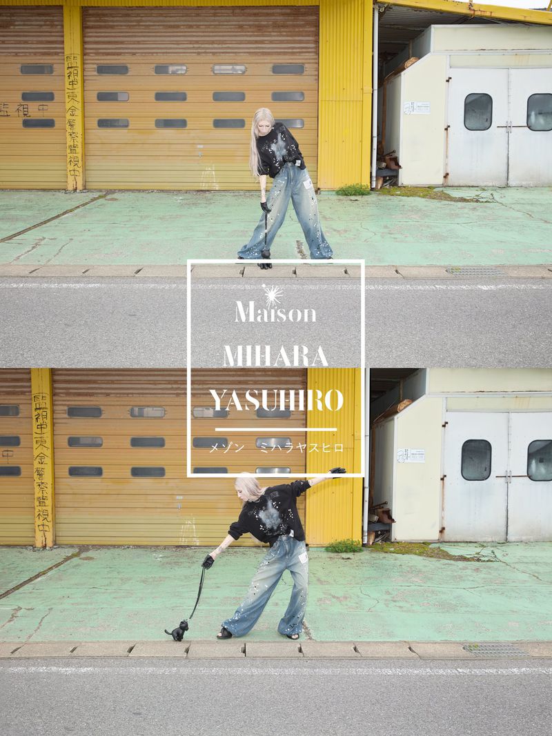 Young woman in casual streetwear holds a dog's leash outside a yellow and white industrial building with a concrete curb.