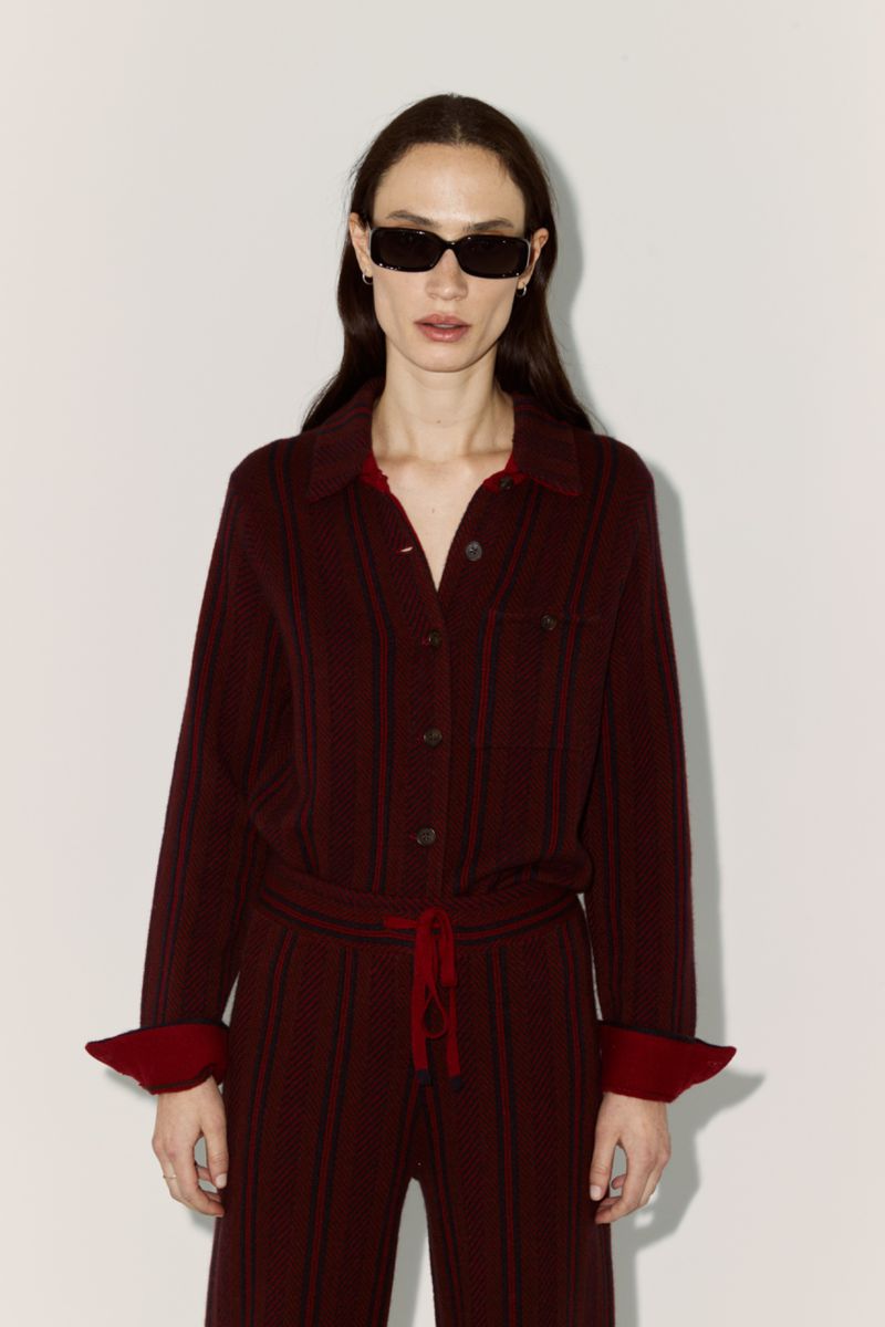 Woman poses in a burgundy striped long-sleeve shirt and pants with sunglasses against a white backdrop in a fashion editorial shot.