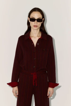 Model Sophie Koella in black sunglasses and a burgundy knit shirt and trousers set against an off-white studio background.