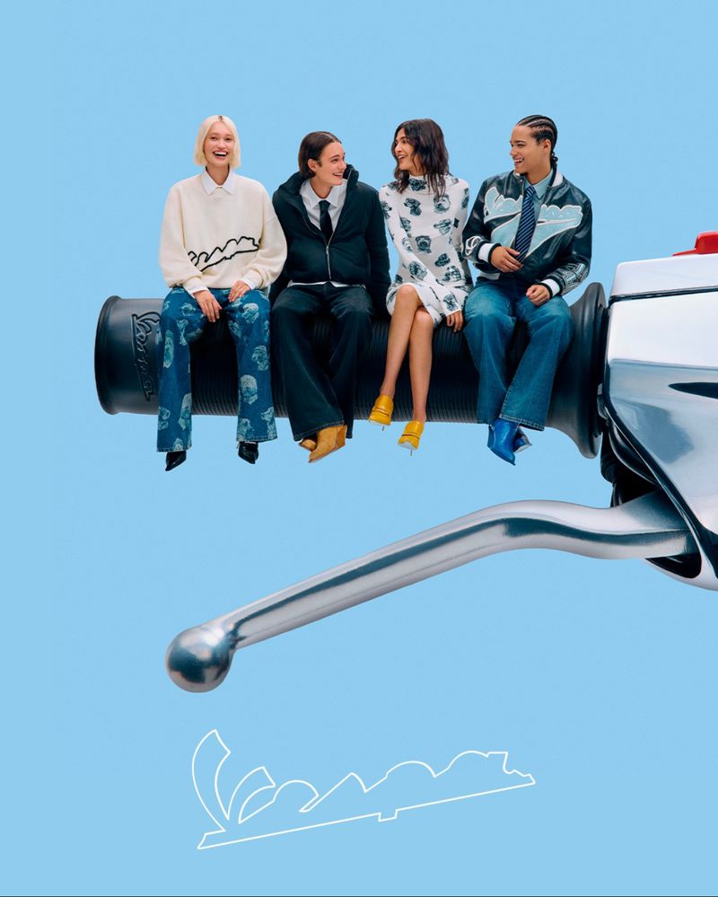 Four stylish women sit on a motorcycle handlebar against a light blue background, showcasing fashion and a unique, playful composition.