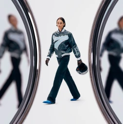 Model wearing a blue leather varsity jacket and holding a helmet between two large chrome mirror frames