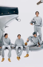 Models in matching grey sweatsuits and tan boots pose on a giant silver scooter against a clean white seamless backdrop.