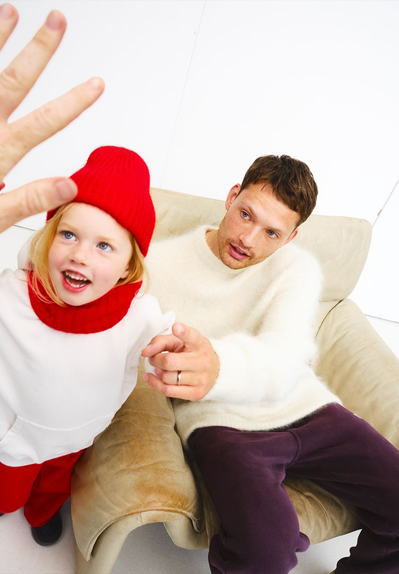 Father and daughter interacting in a brightly lit, minimalist studio setting, with the child in a vibrant red cap and matching bottoms.
