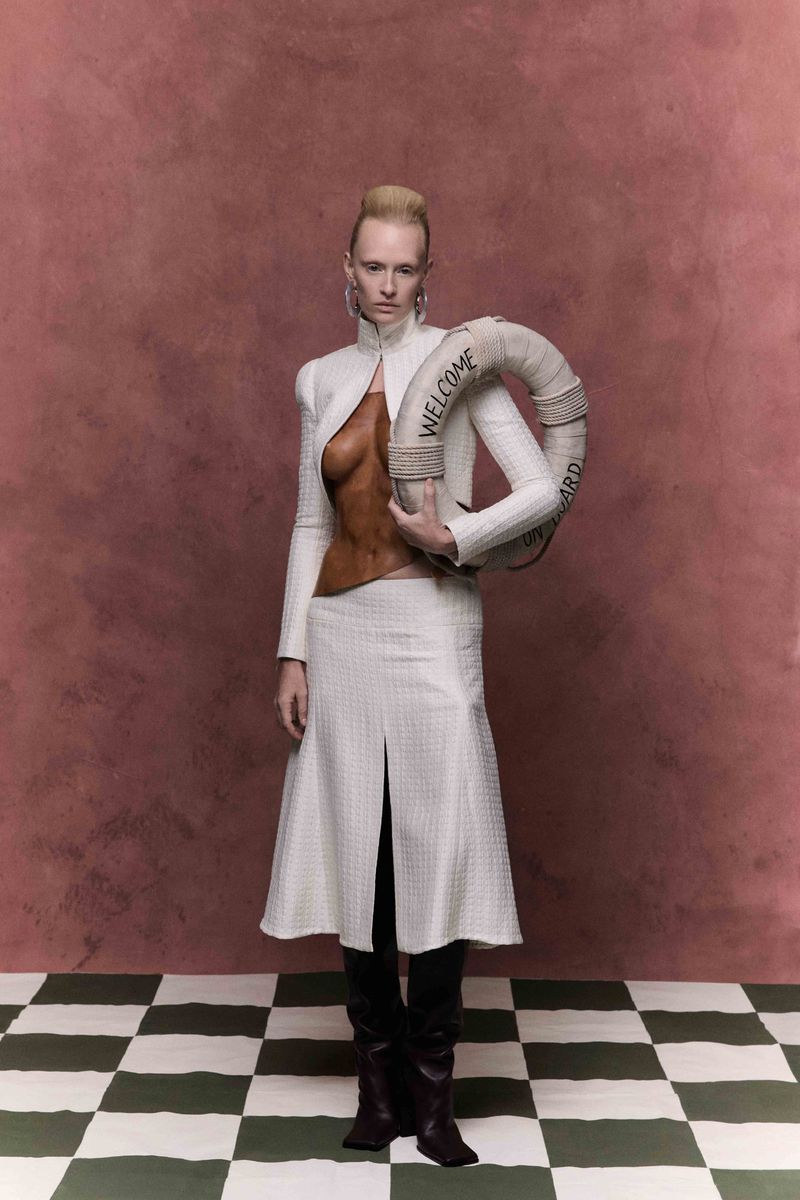 Fashionable woman in a white skirt and jacket posing with a lifesaver in front of a backdrop with a checkered floor.