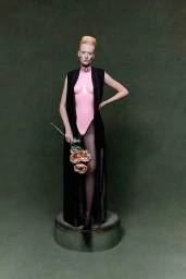 Model standing on a circular pedestal holding flowers, wearing a pink bodysuit and black sleeveless coat.