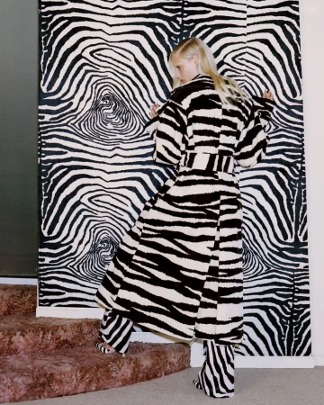 Woman wearing a zebra print robe and pants stands in front of a matching patterned wall. Fashion shot with coordinated black and white.