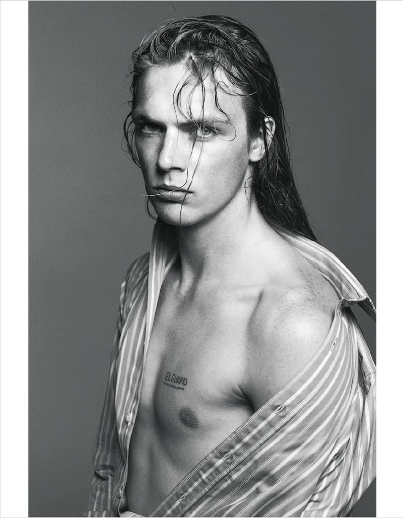 Portrait of a man with long wet hair and striped shirt slipping off his shoulder against a plain grey backdrop