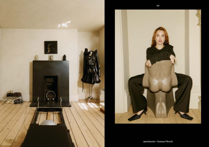 Woman in black outfit sits on a chair in an indoor setting. Room with workout equipment and clothing rack visible in the background.