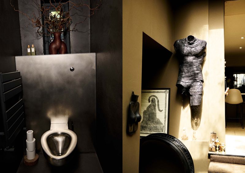 Bathroom interior featuring a toilet with metallic basin, artistic decor including a torso sculpture, and dark neutral color palette.