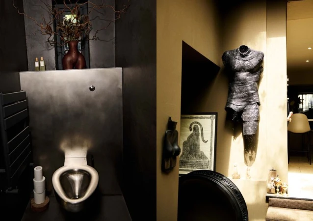Bathroom interior featuring a toilet with metallic basin, artistic decor including a torso sculpture, and dark neutral color palette.