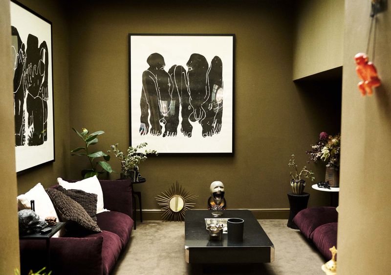 Living room with olive green walls, plum sofas, modern art, and skull decor creates an eclectic and stylish interior design.