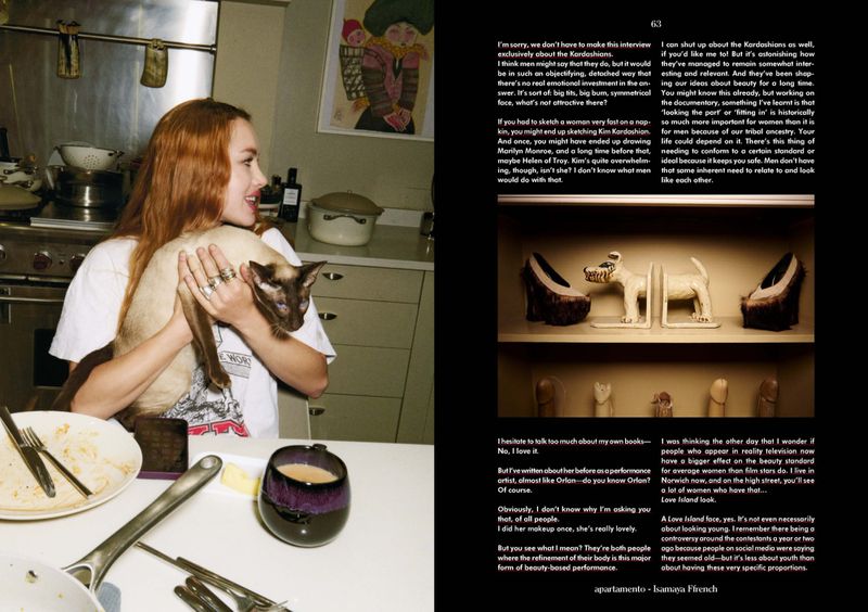 Woman with red hair holds a Siamese cat indoors in a kitchen with a mug on the table, side-by-side magazine layout.