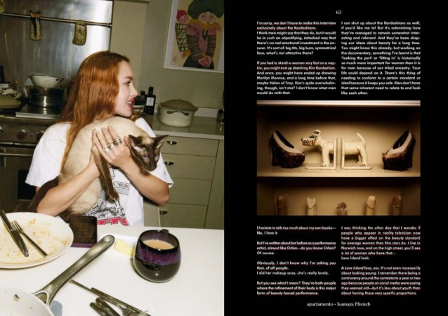 Woman with red hair holds a Siamese cat indoors in a kitchen with a mug on the table, side-by-side magazine layout.