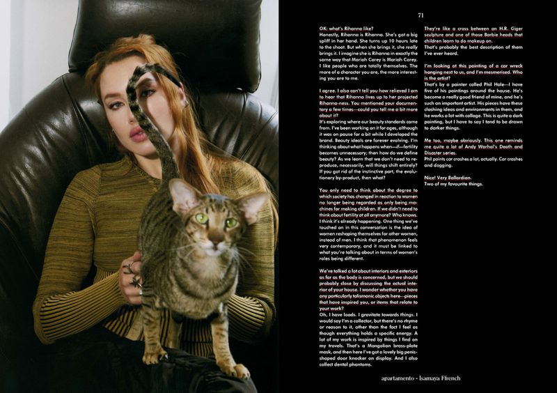Woman in green top sits indoors with an oriental cat, near a magazine spread featuring portraits and text about beauty ideals.