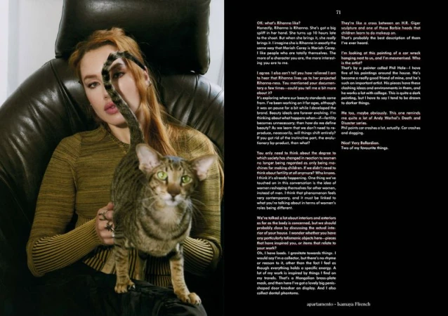 Woman in green top sits indoors with an oriental cat, near a magazine spread featuring portraits and text about beauty ideals.