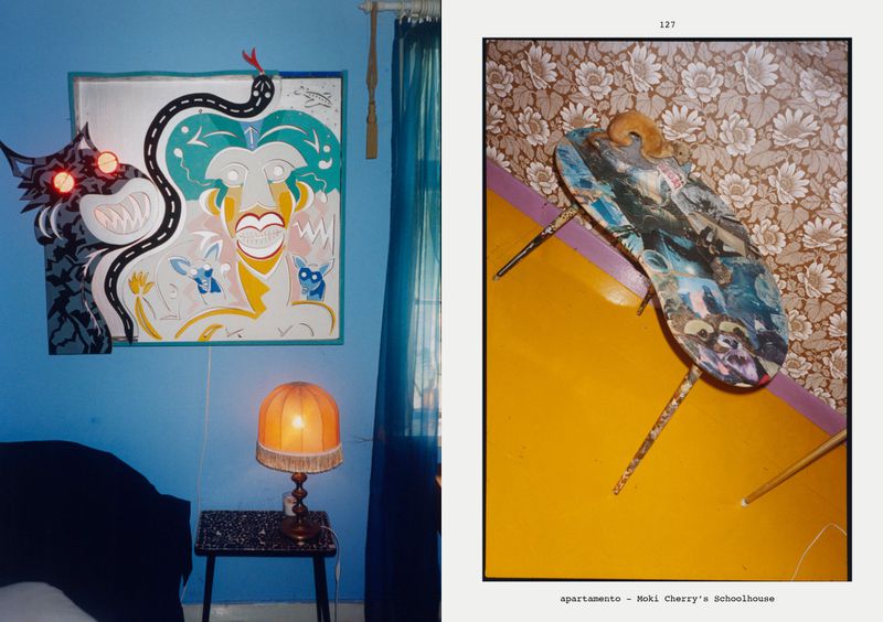 Surreal collage of illustrations on a blue wall with a lamp on a small table, and part of another collage with floral wallpaper.